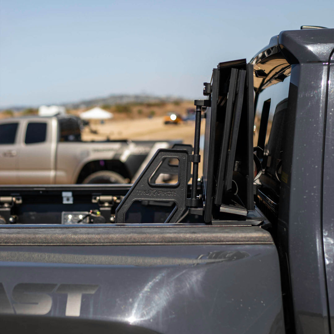 TruxArmor QuadAxis Pro hard folding tonneau cover flipped upright on a Toyota Tacoma, showing the support handle and open truck bed.