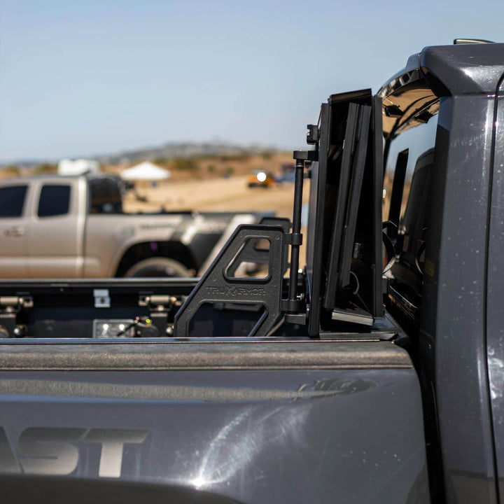 TruxArmor QuadAxis Pro hard folding tonneau cover flipped upright on a Toyota Tacoma, showing the support handle and open truck bed.